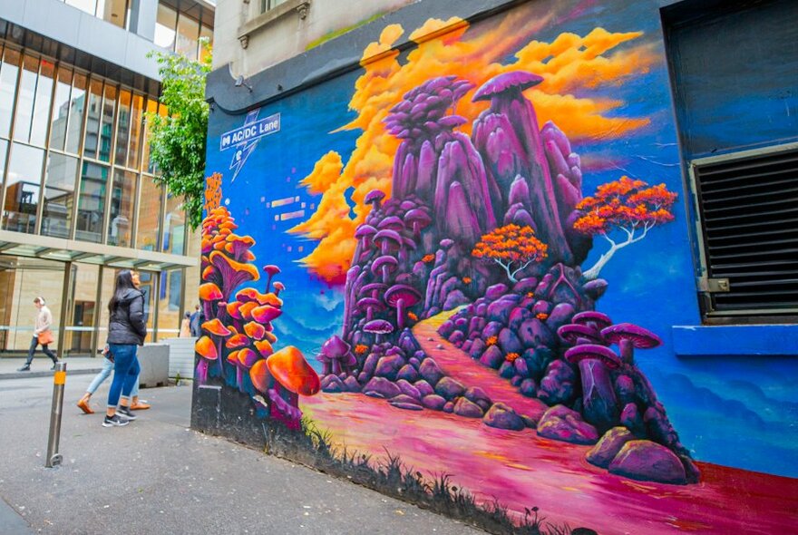 People walking past a mural of a purple mountain with orange mushrooms and clouds.