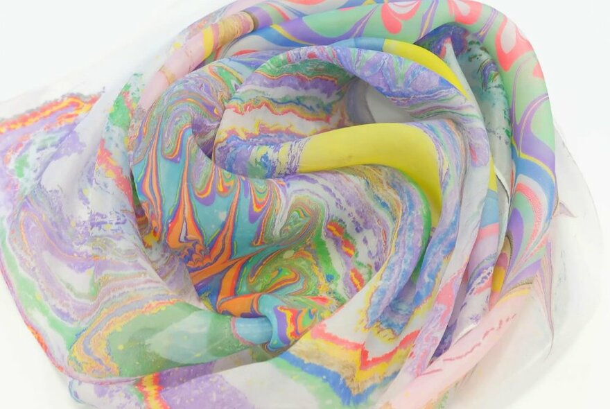 A silk scarf with a soft coloured marbling pattern effect, displayed on a white surface.