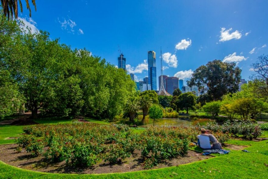 A couple sitting on the grass in a park overlooking the city skyline.