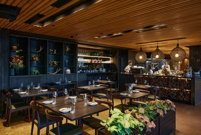 Restaurant interior with dark wood tables, wooden ceiling and plants in a planter.