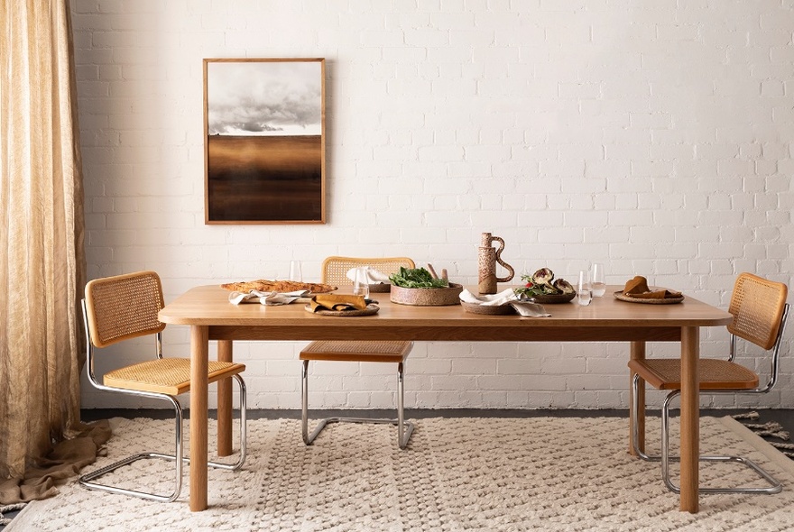 A wooden dining table with three chairs on a woven cream rug.