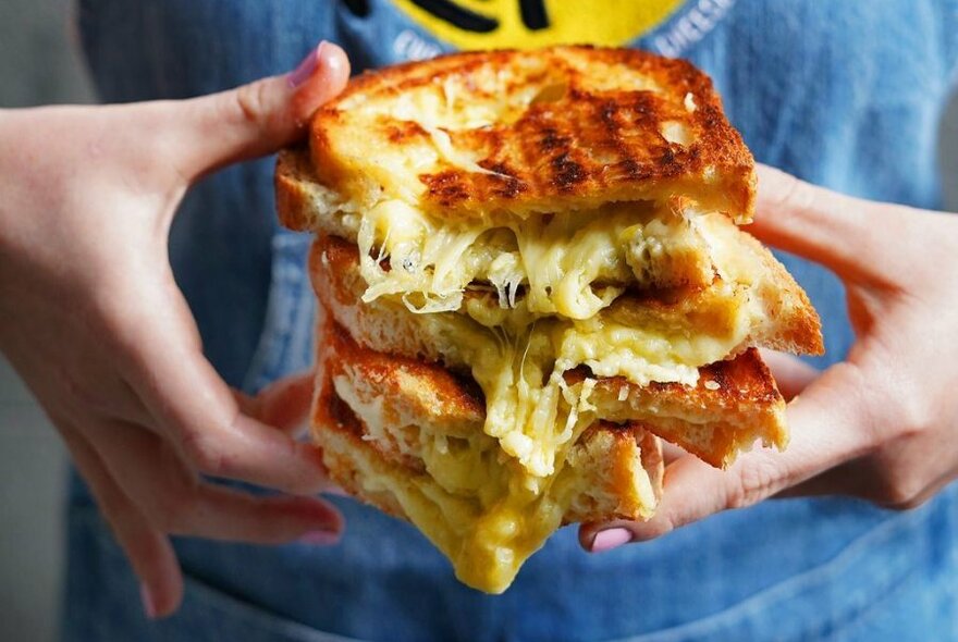 A person holding a stack of toasted cheese sandwiches.