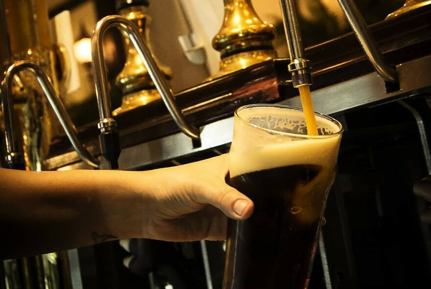 Bartender's hand holding a glass being filled with Guinness on tap.