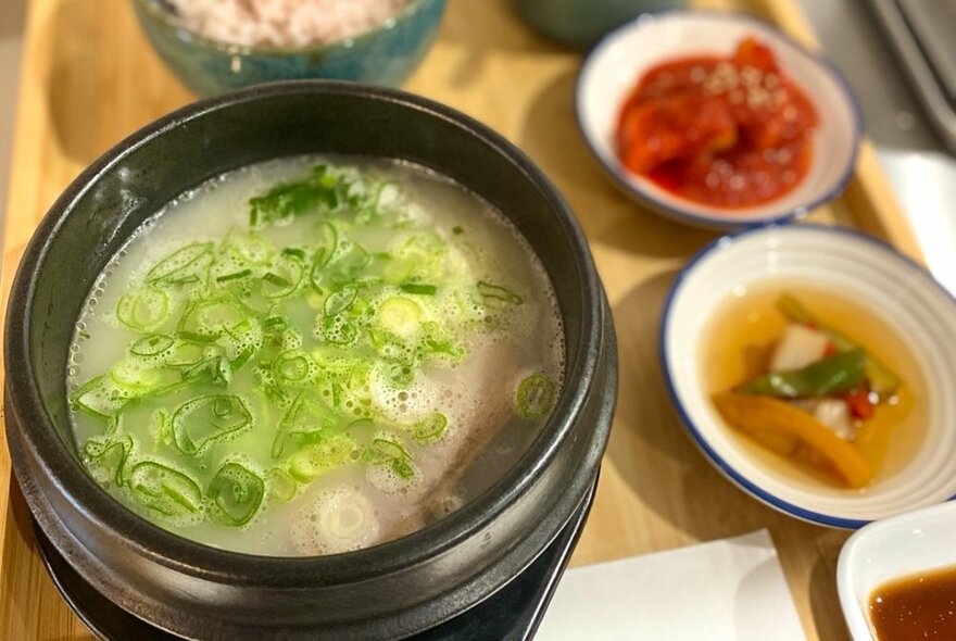 Korean soup bowl with scallions, and smaller bowls with garnishes to the side.