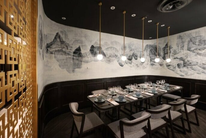 A large restaurant table set for dinner with pendant lights, gold room divider and wallpaper