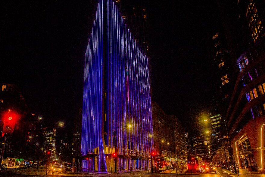 An angular building on a city corner illuminated blue at night.