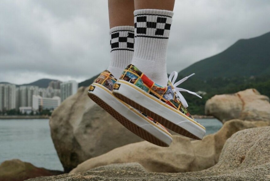 Colourful sneakers and black and white socks, slightly off the ground with rocks and water background.