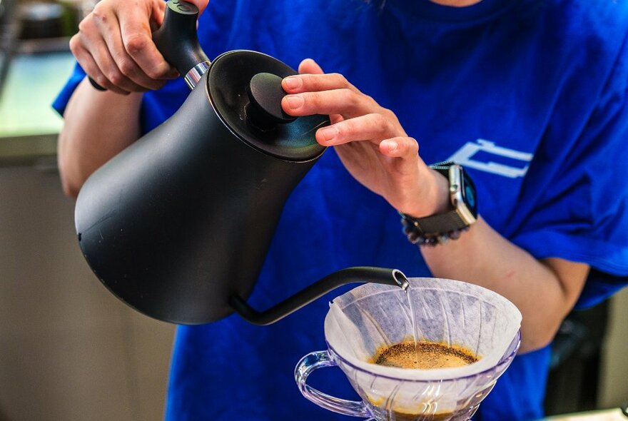 A barista pouring water through a coffee filter. 