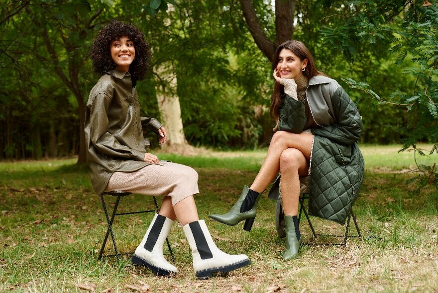 Two women sitting on chairs outside wearing chunky boots. 