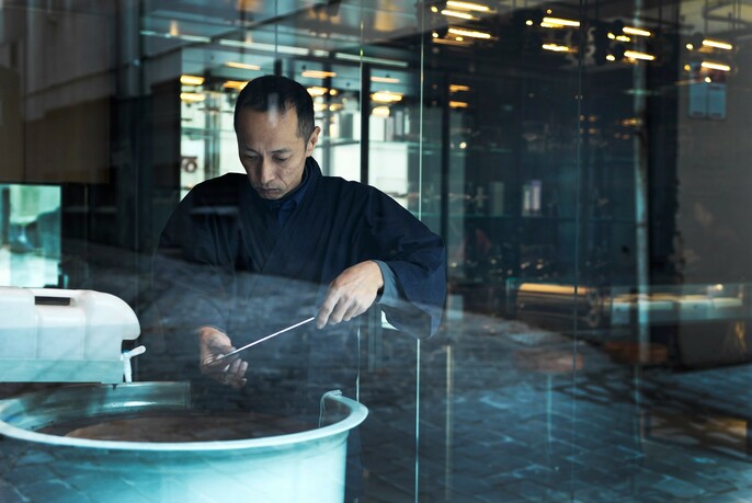 Japanese knife-sharpener honing the blade of a knife in a circular large pot.