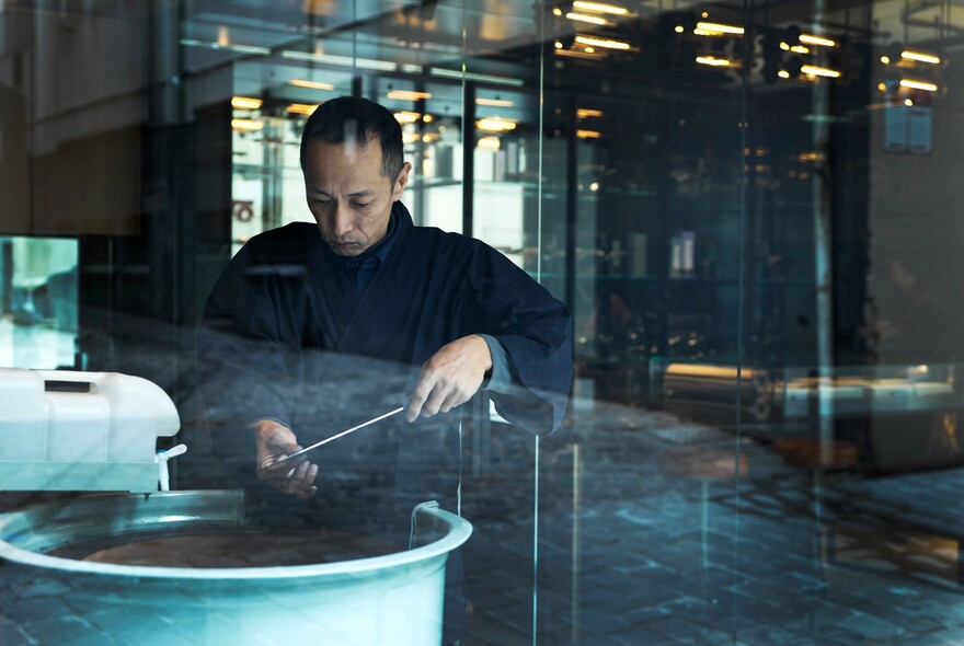 Japanese knife-sharpener honing the blade of a knife in a circular large pot.