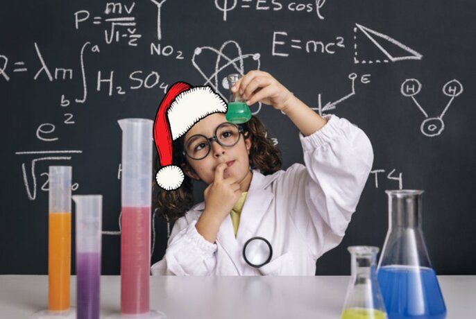 Child in a white lab coat and glasses and wearing a superimposed red Santa hat, holding up a test tube of liquid in a laboratory type setting, standing in front of a chalkboard with scientific formulas written on it.