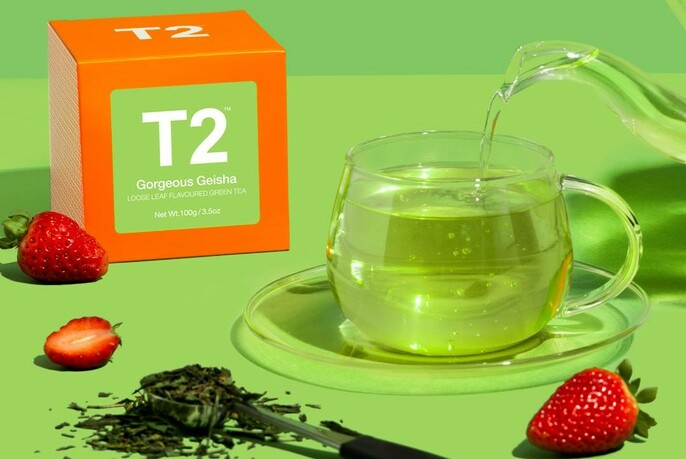 Packet of T2 tea with a glass of herbal tea and strawberries.