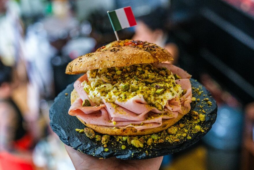 A focaccia sandwich filled with mortadella, cheese and pistachios, and topped with a small Italian flag.