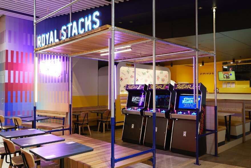Exterior of Royal Stacks burger cafe at Emporium showing three arcade style gaming machines and tables and chairs.