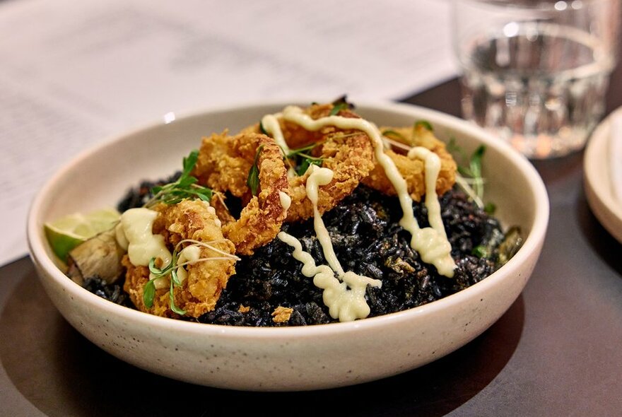 A black rice dish topped with fried calamari.