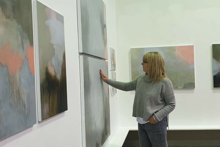 Woman closely examining painted artworks on a gallery wall.