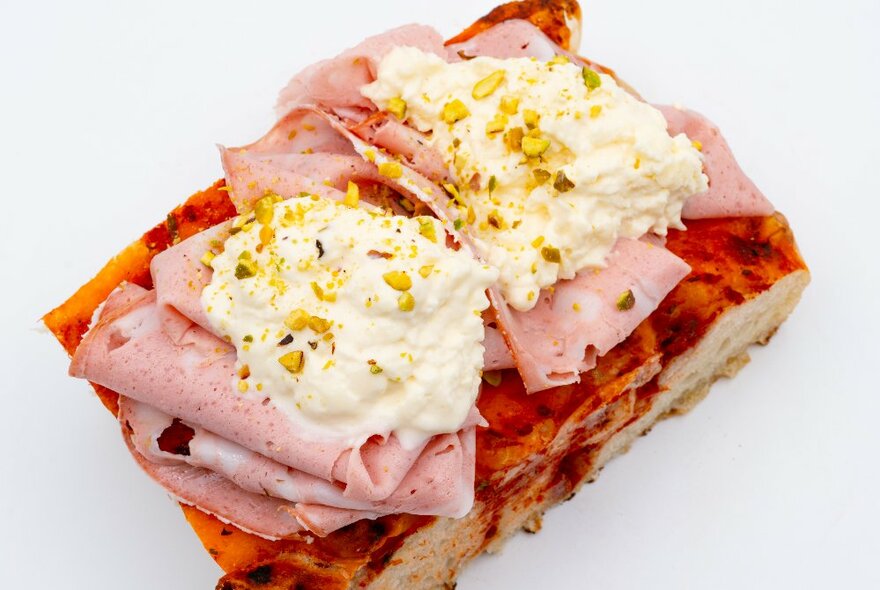 Open pizza sandwich with sliced deli meats and creamy hummus with chopped nuts sprinkled on top.