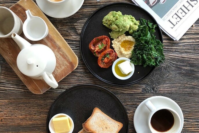 Table setting with avocado breakfast dish, toast and butter, coffee and tea.