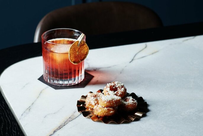 A table with a cocktail and parmesan doughnuts.