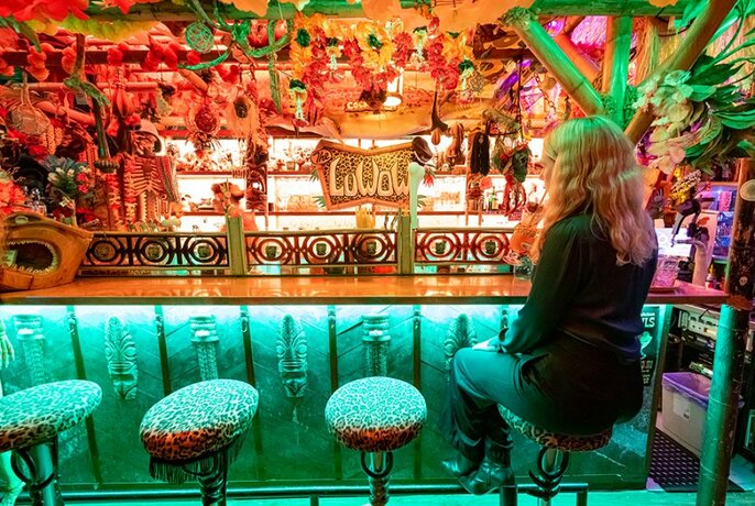 A woman sitting at the bar in a colourful tiki bar.