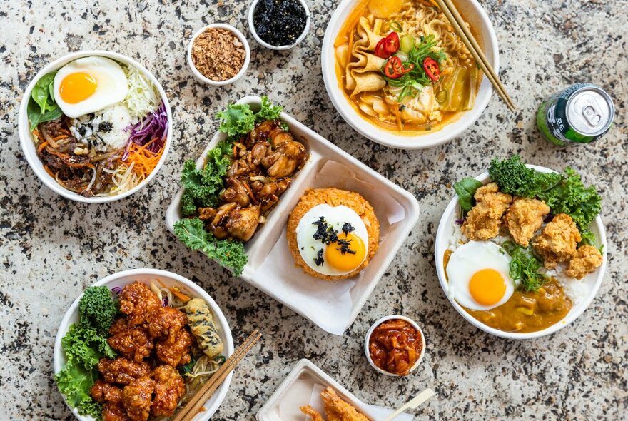 Looking down on a table with many bowls of Korean chicken and condiments. 