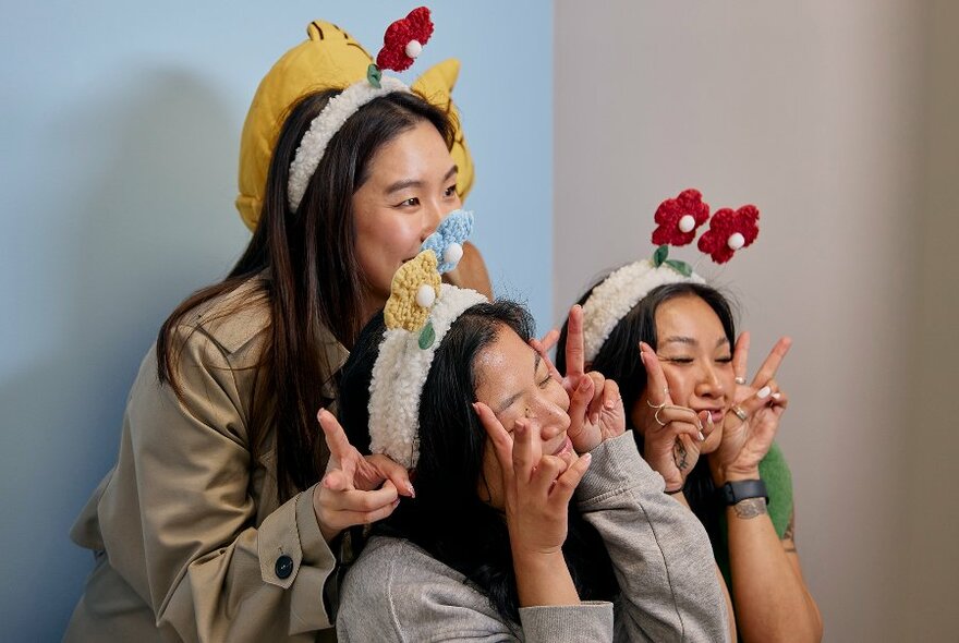 Three girls posing and holding up their hands in peace signs while wearing flower headbands.
