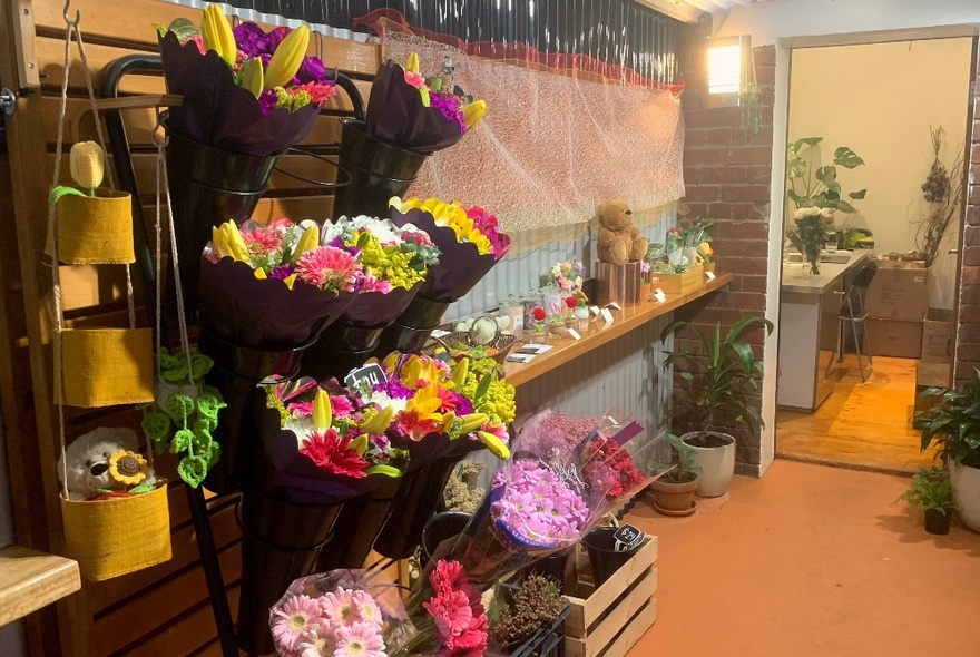 Small shop space with floral arrangements hanging in buckets on a wall, and a shelf of other assorted gifts.