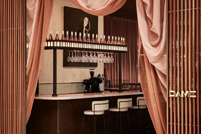 Dame's bar with seating and drinks behind pink draped curtains.