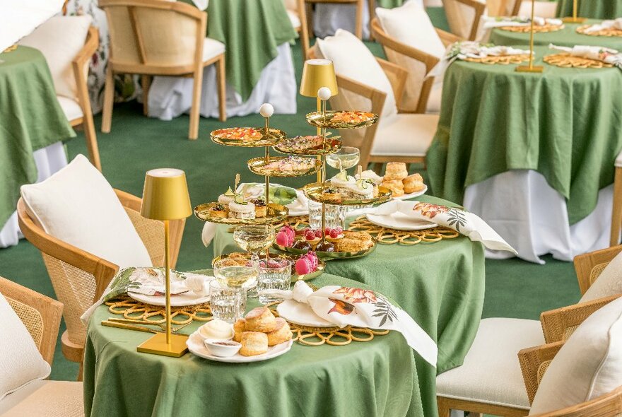 Rows of cafe tables draped with green tablecloths and topped with tiered platters of scones, cakes and hors d'oeuvres.