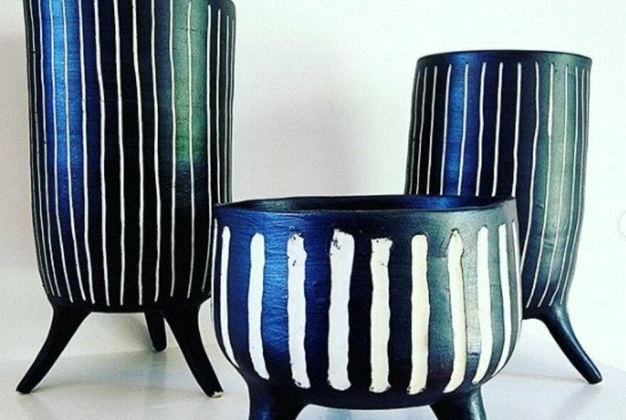 Three black and white striped pottery vases or plant pot holders on a white table.