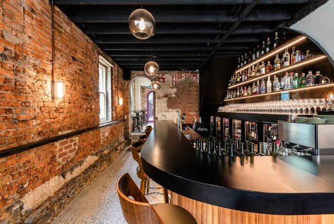 Interior of bar showing exposed brick wall, curved bar area, bar stools, and shelves bottles of alcohol behind the service area.