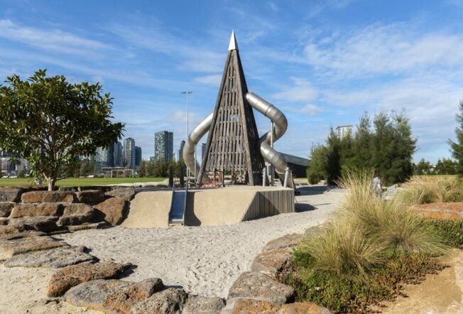 A rocket ship shaped double slide with the Melbourne city skyline in the background. 