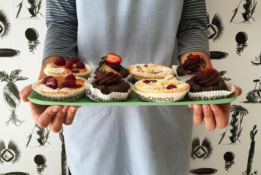 Person holding a tray of sweet chocolate and strawberry pastries.