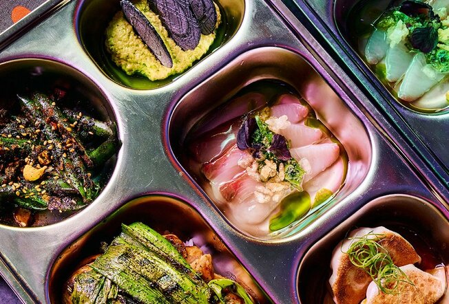 A close up of a silver bento box filled with fish, dumplings and vegetables.