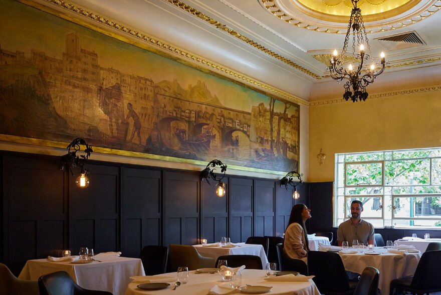 A couple dining under a mural in a fine dining restaurant.