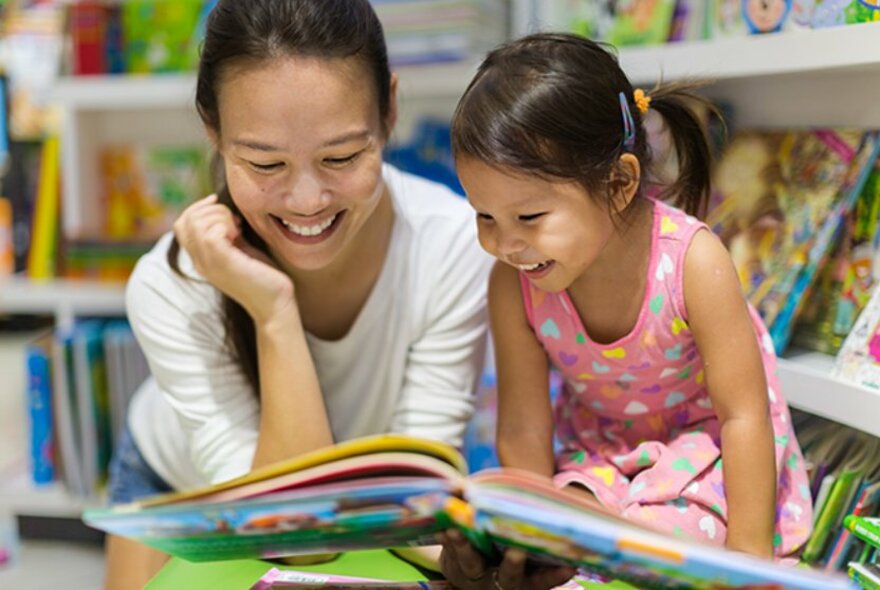 A woman and a young girl leaning over a storybook and laughing. 
