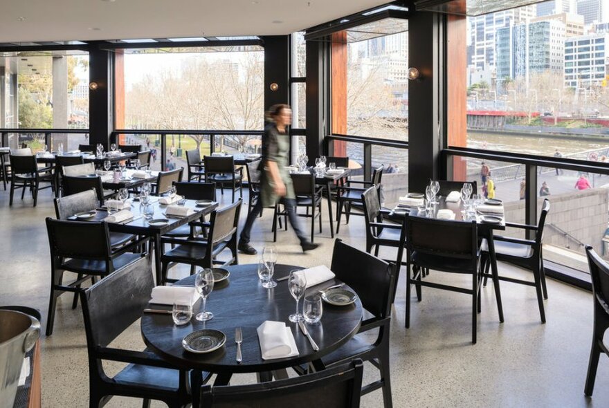 A restaurant interior overlooking the river with floor to ceiling windows.