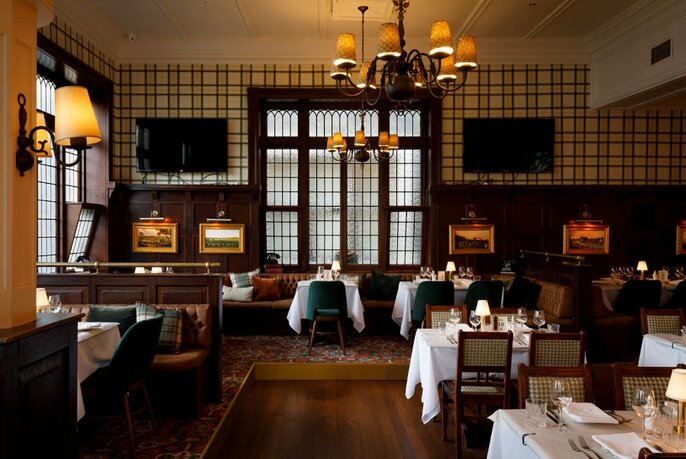 Bar Moubray interior with dark panelled walls, soft lighting, white linen-covered tablecloths,and tables set for dinner service.