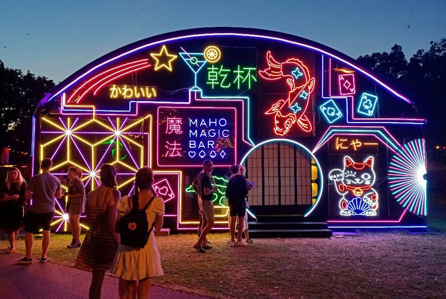 Maho Magic Bar installation with neon lights and people at dusk.