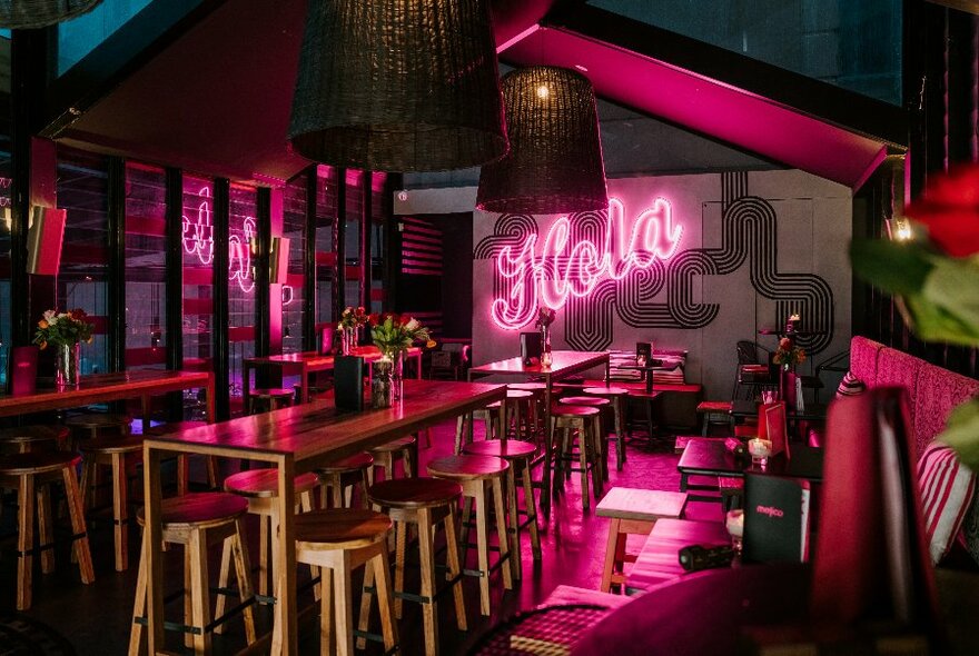 Intimate bar with pink neon lighting, a central counter with stools and banquet seating.