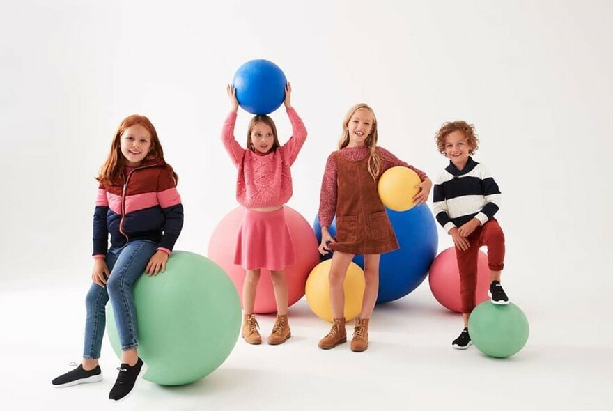 Four children playing with oversized rubber balls in a white studio.
