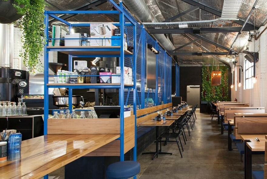 Warehouse cafe interior with blue metal shelves, wooden tables and chairs, polished concrete floor.