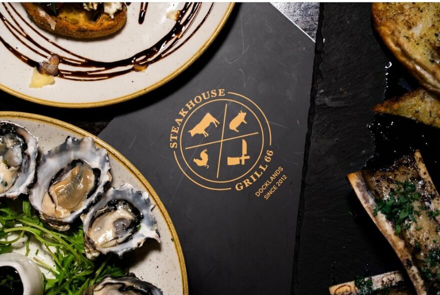 Looking down on a segment of a plate of oysters with a steakhouse logo on a menu.