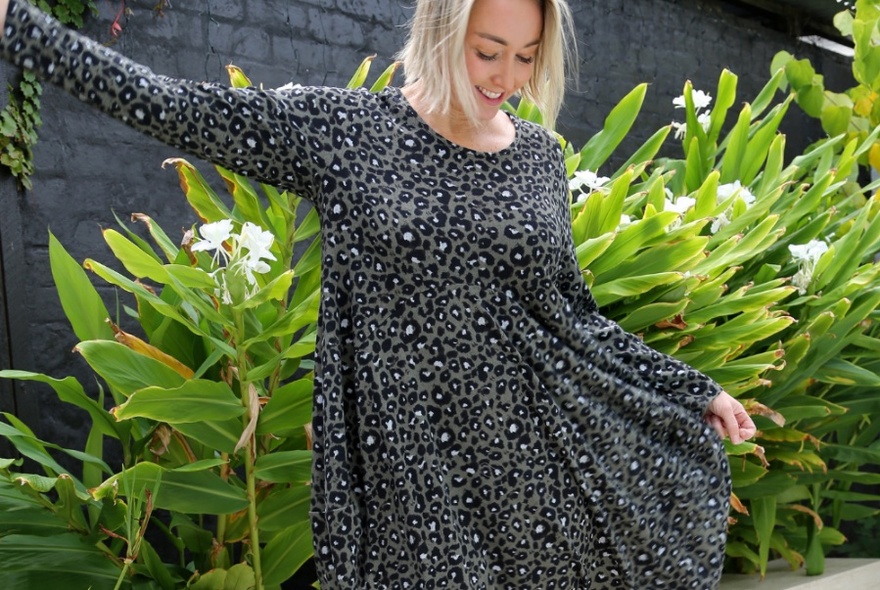 Smiling woman with a blond bob haircut looking down, twirling while modelling an animal print long sleeved dress.