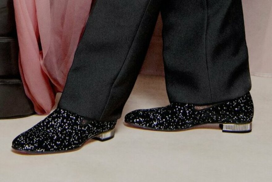 Male feet encased in dark coloured sparkling loafers.