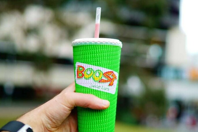 A hand holding up a bright green Boost Juice cup with a straw.