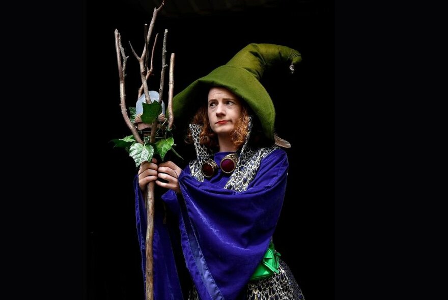 A wizard performer wearing a big green hat and holding a wooden broom.