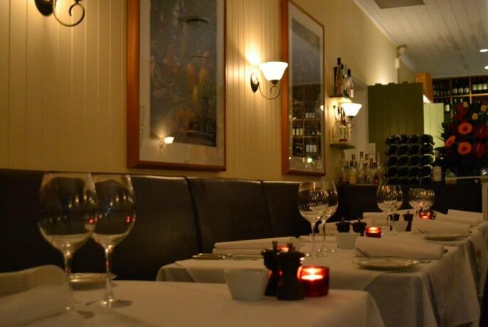 The cosy dining room of Sud restaurant with candlelit tables with white tablecloths set for dinner. 