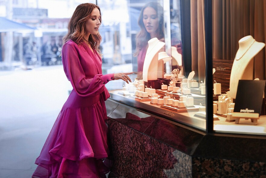 Woman in a pink dress looking into jewellery shop window.